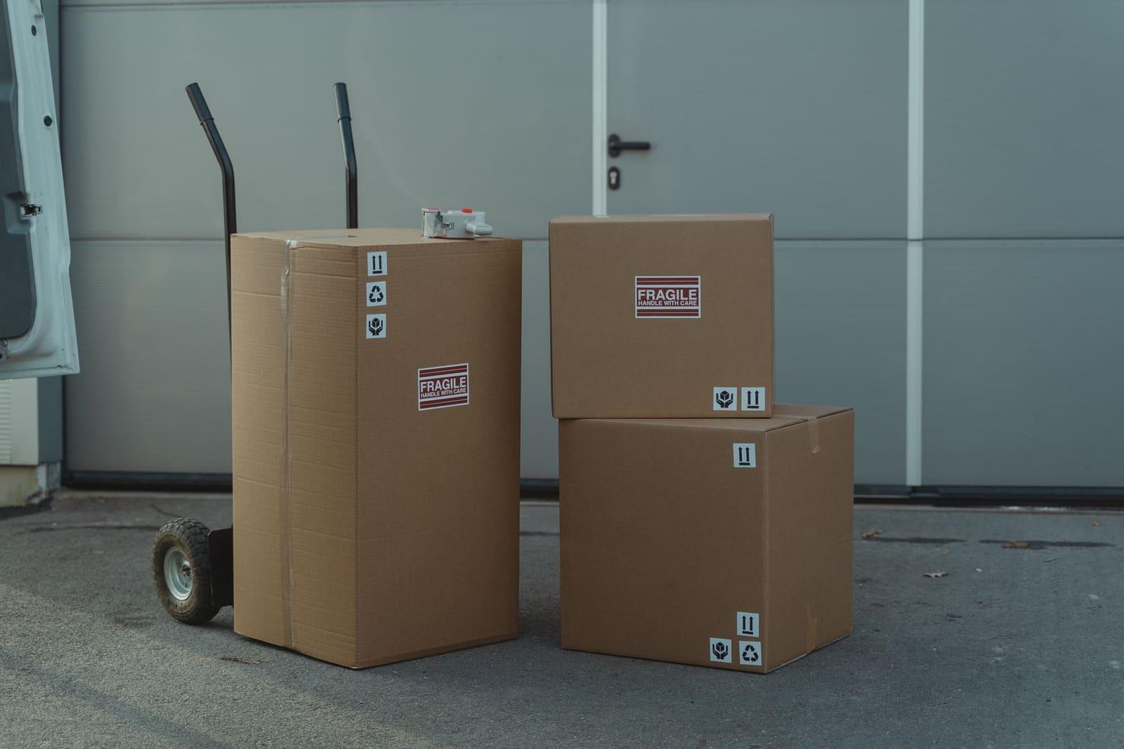 Packed cardboard parcels on a sack truck beside a van, ready for dispatch.